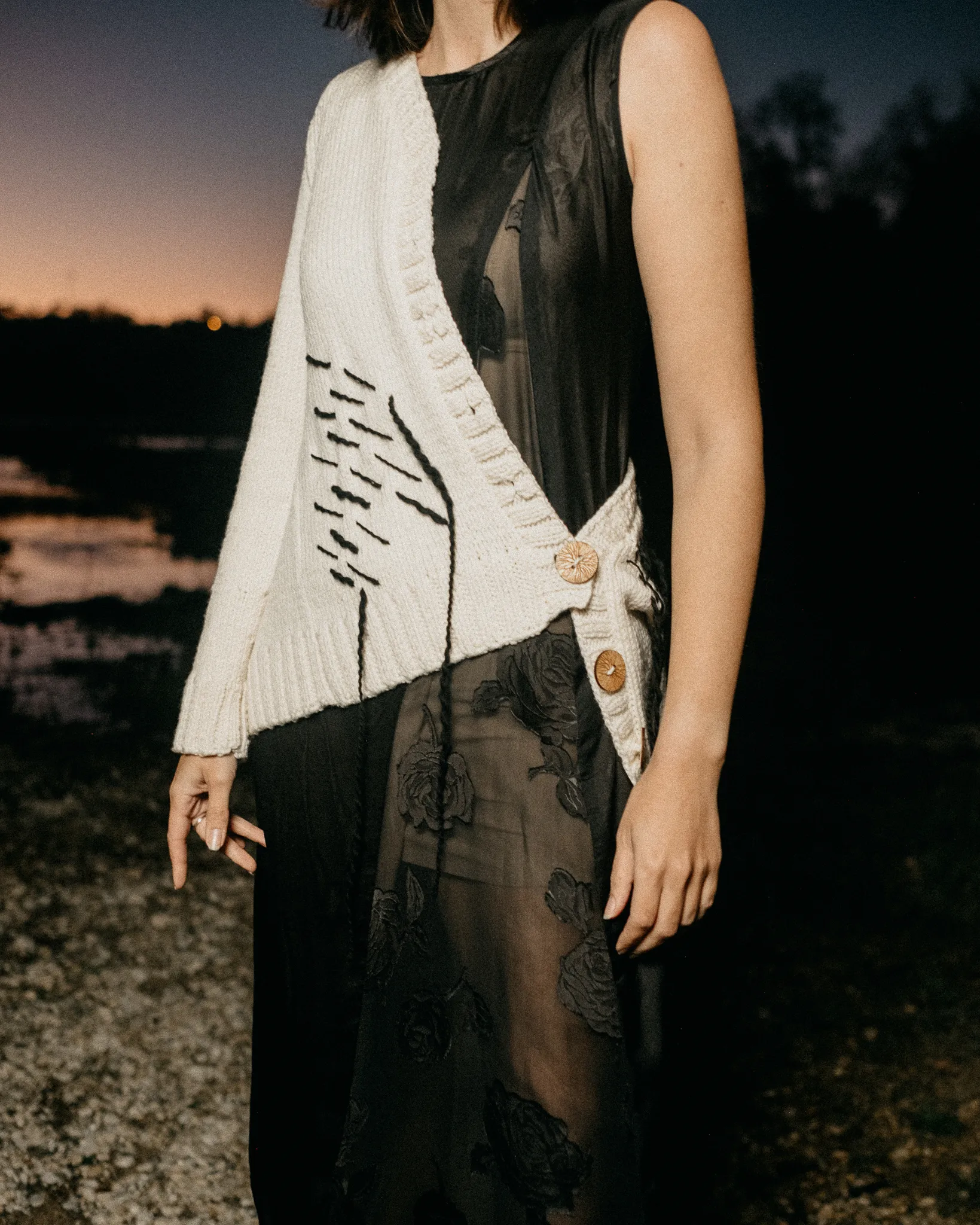 Model in Looking Friday cream Italian merino wool Abstract Cardigan side-buttoned over a sheer black floral silk dress.