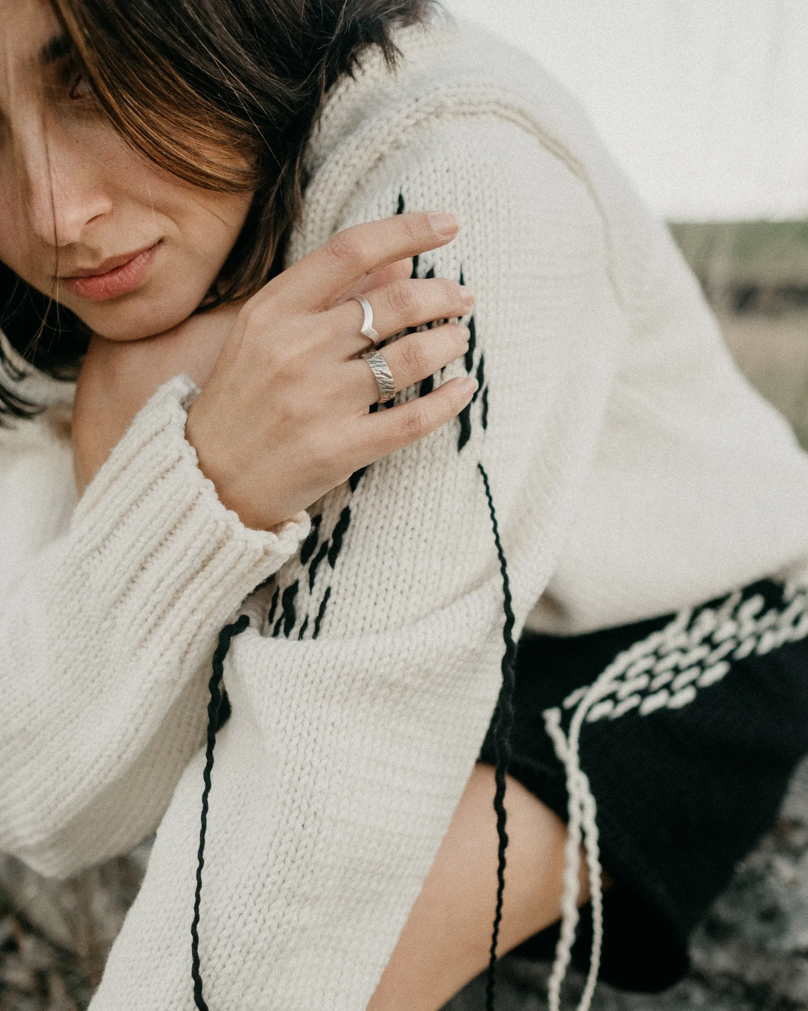 Portrait detail of Looking Friday cream Italian merino wool sweater sleeve featuring ribbed cuffs and black hand-stitched embroidery.