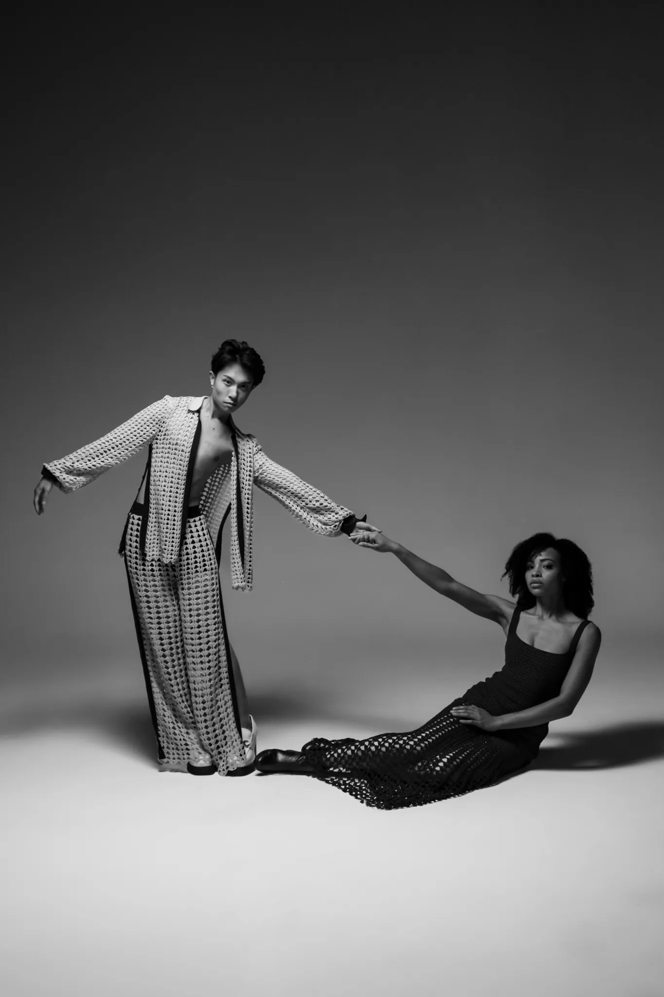 Two models in Looking Friday crochet outfits: a fan-pattern shirt and wide-leg pants paired with a dark navy bodycon dress.